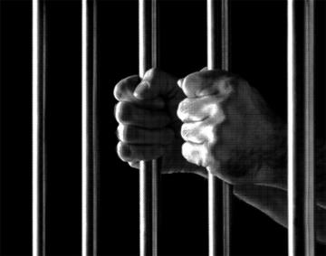 black and white treated image of a prisoner's hands behind bars 