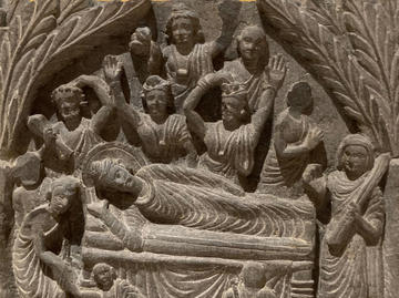 photo of a stone carving of the Buddha's death with reclining figure surrounded by people.